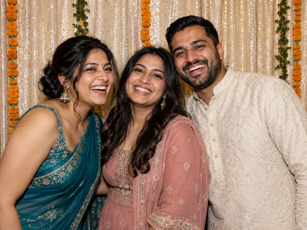 Three guests in traditional South Asian attire laughing in front of a sequin and marigold photo booth backdrop