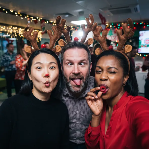 Three coworkers in reindeer antlers pulling silly faces at an office holiday party photo booth