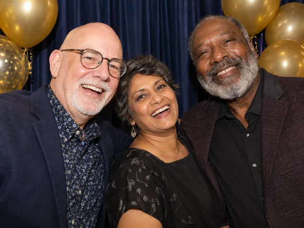 Three friends laughing at a milestone birthday photo booth with gold balloons and a navy backdrop