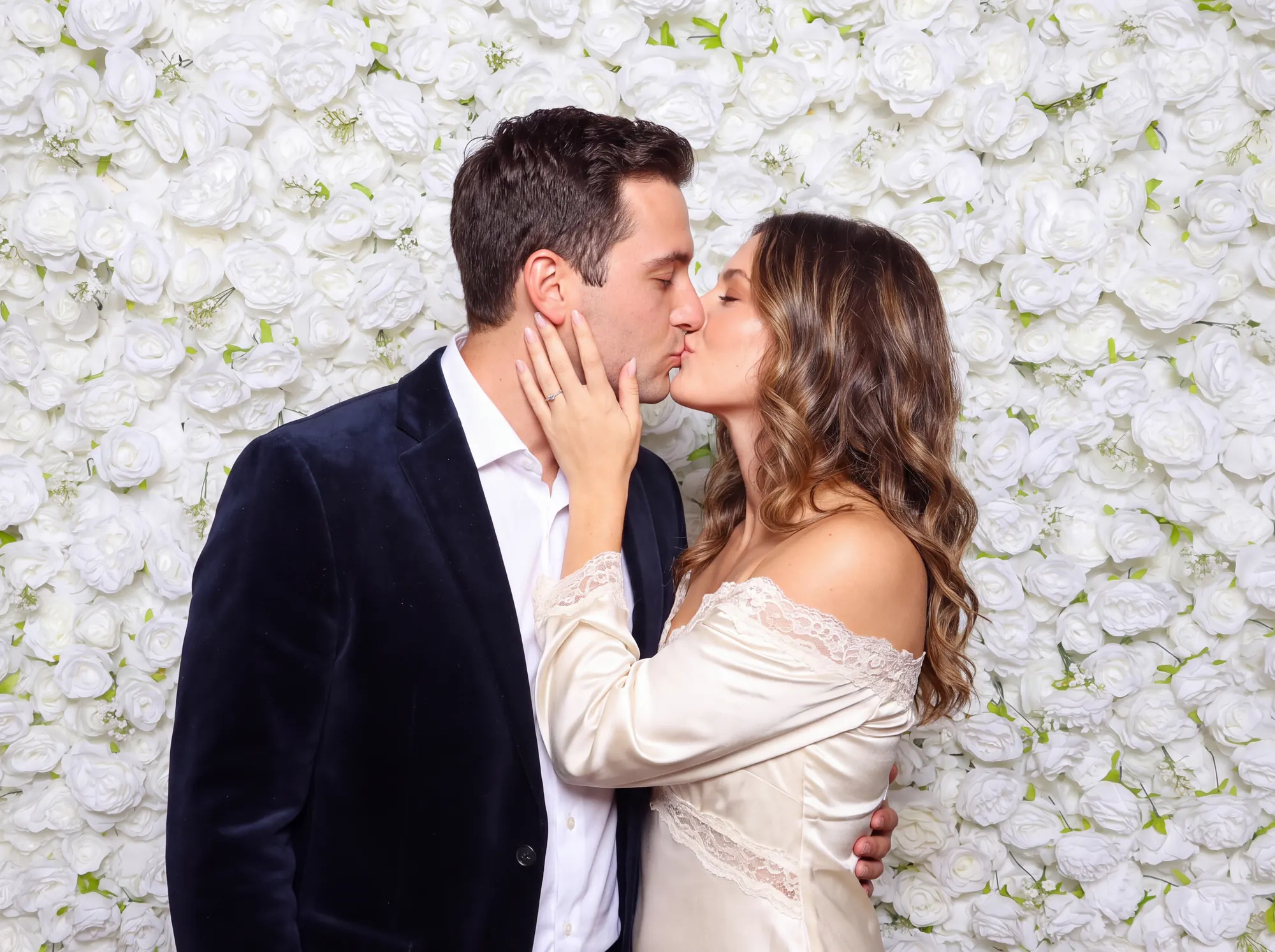 Couple in front of a white flower wall at a wedding photo booth